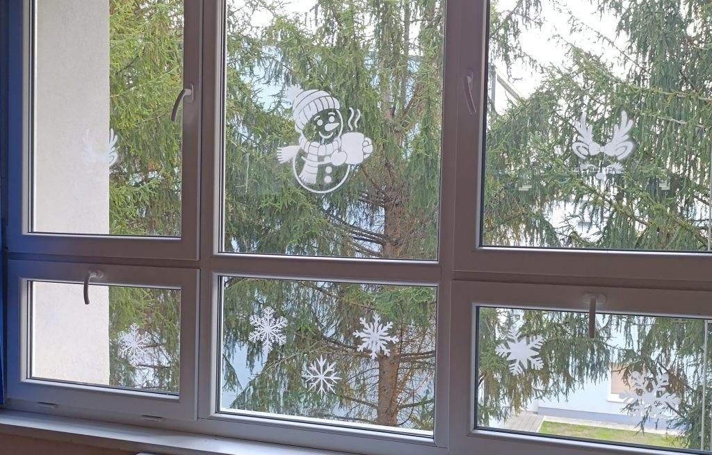 Božićne šablone na prozorima — snjegović, sob i pahuljice napravljene umjetnim snijegom.
